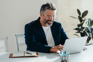 Happy Bearded Businessman Working Happily on Laptop in a Bright Office